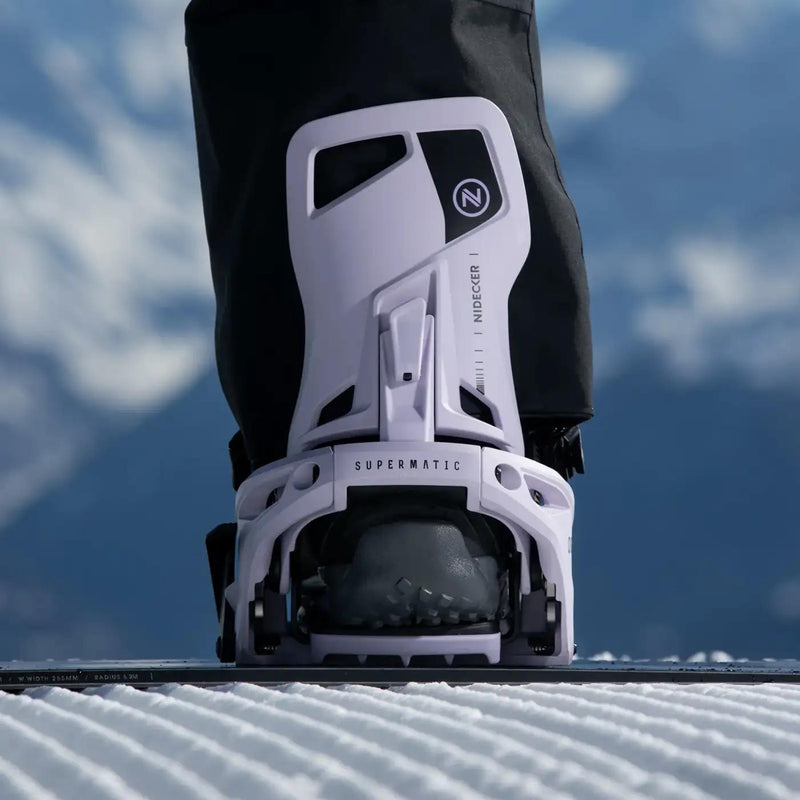 A person standing on a snowboard with their foot in a white binding with a Nidecker logo on a snowy hill. 