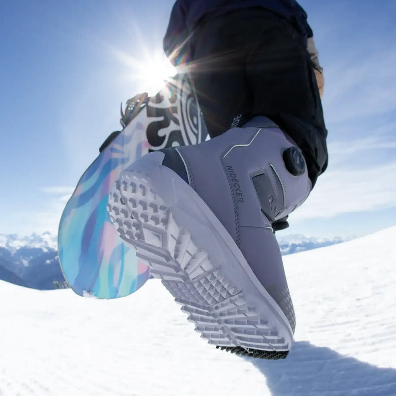 Man with a snowboard wearing a pair of grey and white snow boots on a snowy mountain.