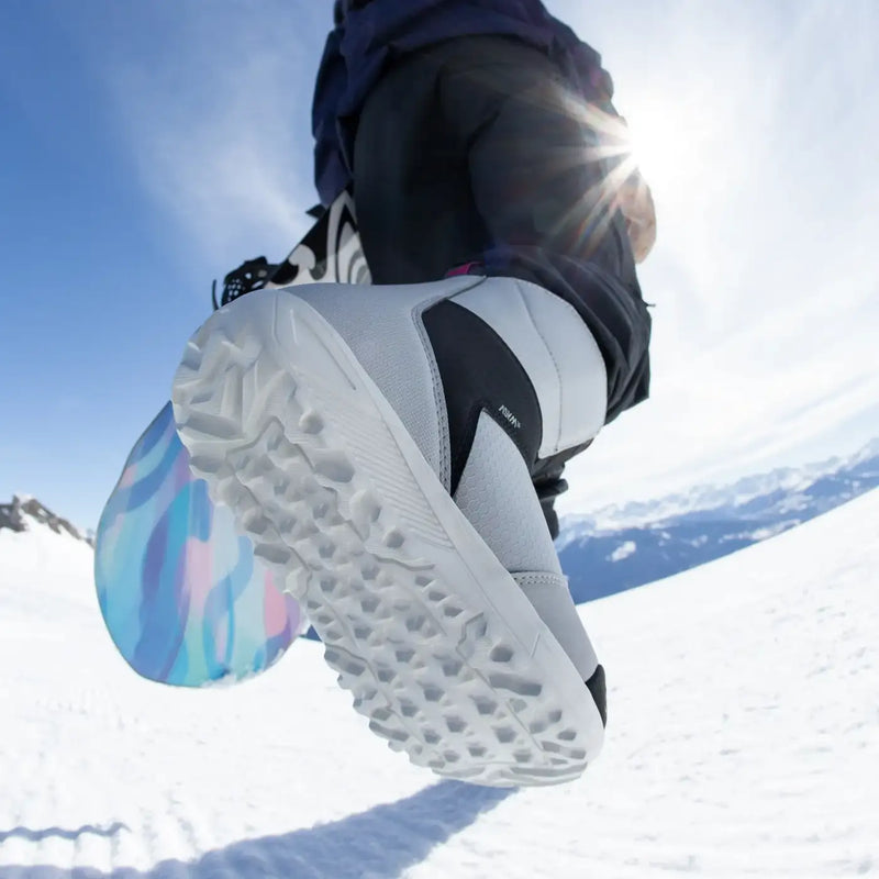 Person carrying a snowboard on a snowy mountain wearing a white snowboot with black accents. 