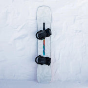 White snowboard with black bindings and a Nidecker logo against a snowy background.