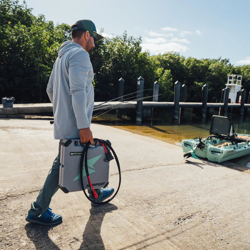 A man carrying a grey battery pack to his boat on a sunny day with a dock in the background.