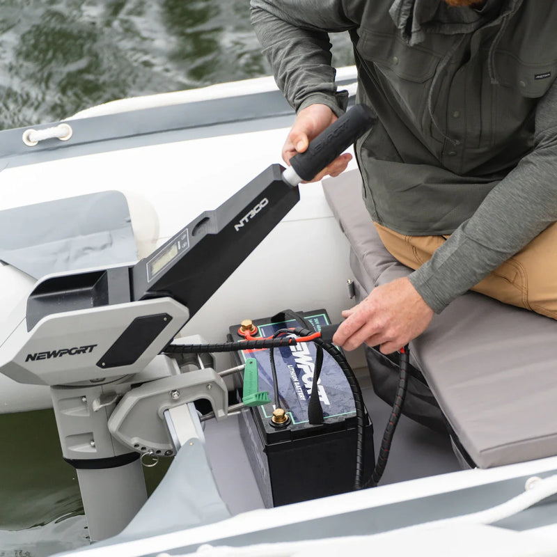 A man attaching a battery pack to the motor of his boat with water in the background.