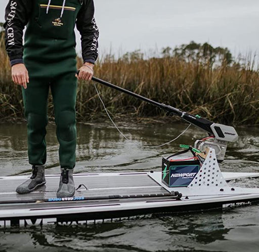Close up image of a man using a tiller extension handle paddling his boat in a marsh with tall grass in the background.