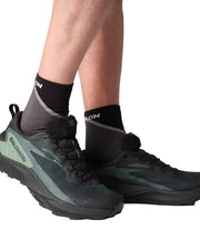 Person wearing black and green hiking shoes with 'Salomon' branding on a light gray background