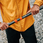 Person wearing a yellow jacket holding a black and orange rod with a brand logo.