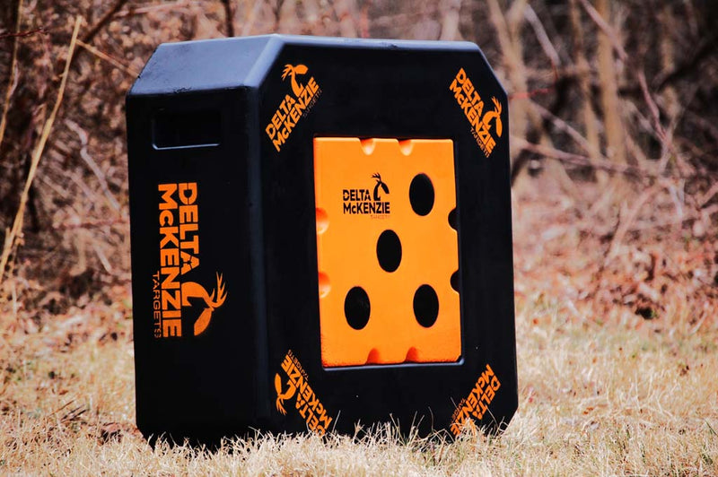 Black square archery target with orange center with Delta McKenzie logo in the middle of a field. 