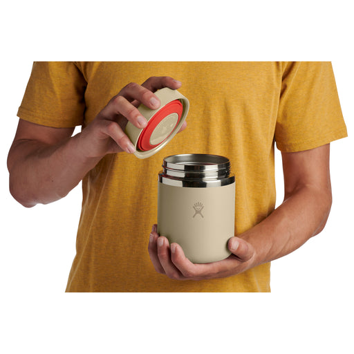 Person holding a beige and red insulated mug with a logo on a white background