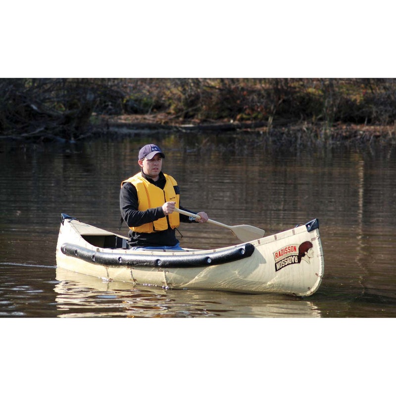 A man wearing a yellow life vest sits in a beige and black canoe on a body of water, holding a paddle. The canoe has a visible 'Plattner Discovery' logo on the front.