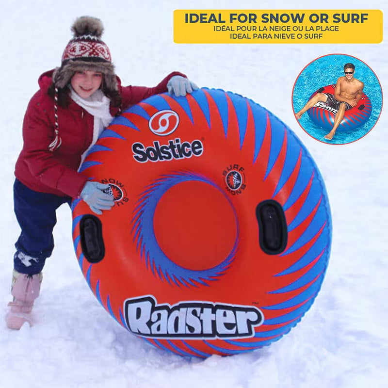 Child standing on a snowy mountain holding up a red inflatable tube with blue accents with a text that reads "ideal for snow or surf" showcasing it's versatility. 