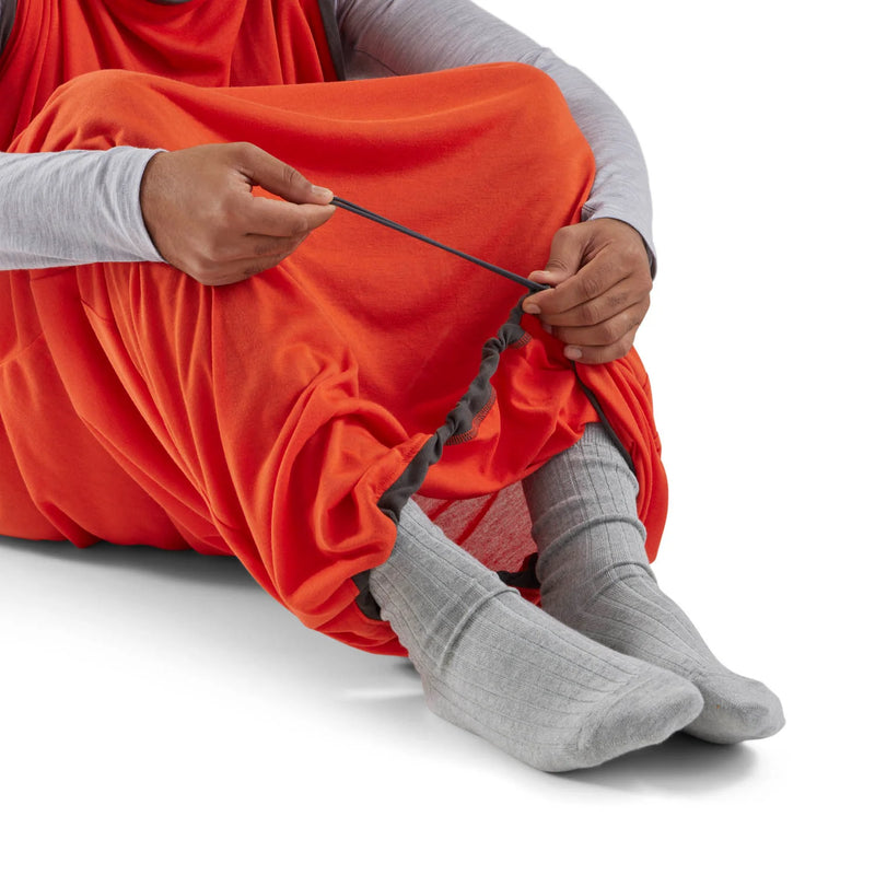 Person wearing an orange garment and gray socks sitting on a white background