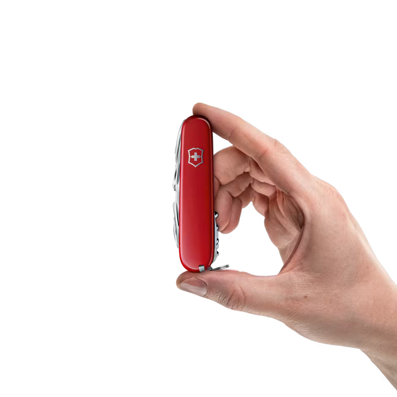 Hand holding a red colored multitool featuring a Victorinox logo against a white background. 