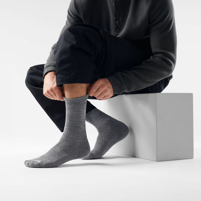 Person wearing gray socks sitting on a white cube against a light background