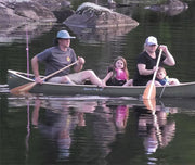 Family of 4 paddling their green canoe down a calm stream with rocks in the background.