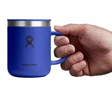 Hand holding up a small blue travel mug with a Hydroflask logo on it on a white background.