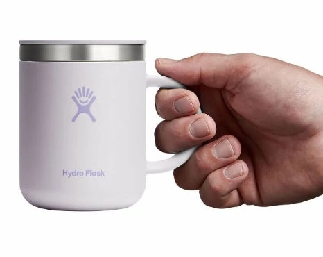 Hand holding up a small light pink travel mug with a Hydroflask logo on it on a white background.