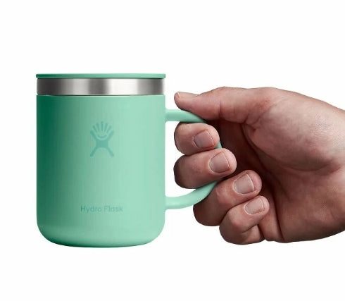 Hand holding up a small green travel mug with a Hydroflask logo on it on a white background.
