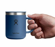 Hand holding up a dark blue travel mug with a Hydroflask logo on it on a white background.