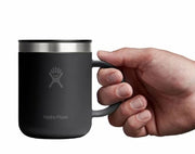 Hand holding up a small black travel mug with a Hydroflask logo on it on a white background.