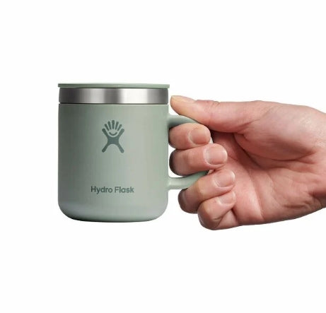 Hand holding up a small light green travel mug with a Hydroflask logo on it on a white background.