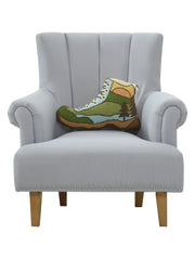 Boot shaped pillow with a forest pattern on it resting on a gray chair against a white background. 