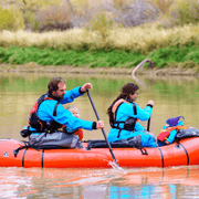 Family paddling their red inflatable kayak in a calm lake.