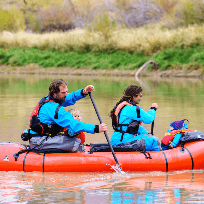 Family paddling their red inflatable kayak in a calm lake.