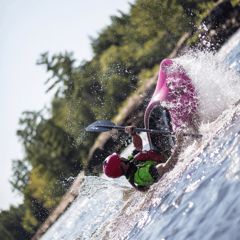 Person kayaking through a waterfall with trees in the background