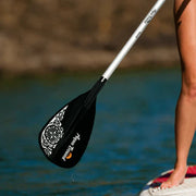 Person holding a black and white paddle over a body of water.