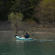 Man paddling down a river in a blue inflatable kayak with white accents. 
