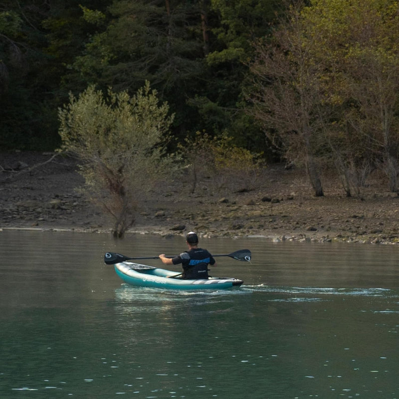 Man paddling down a river in a blue inflatable kayak with white accents. 