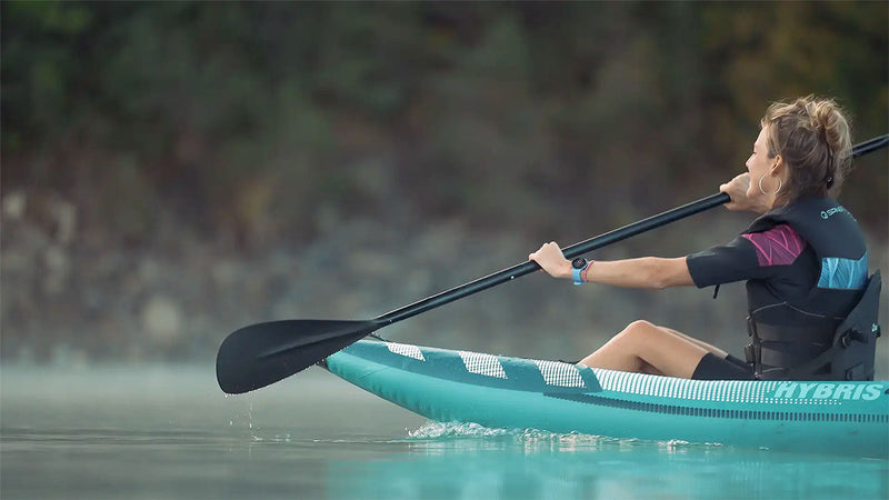 Woman rowing a blue and white colored inflatable kayak down a river using a black paddle.