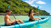 A man and a woman in a blue and white colored inflatable kayak rowing with blue and black paddles down a river.