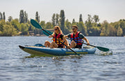 Man and woman in a blue inflatable kayak with yellow accents paddling through a lake. 