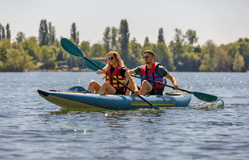 Man and woman in a blue inflatable kayak with yellow accents paddling through a lake. 