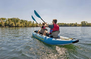 A man and woman in a blue inflatable kayak with yellow accents in a lake. 