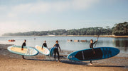 Four people with paddleboards on a beach near water