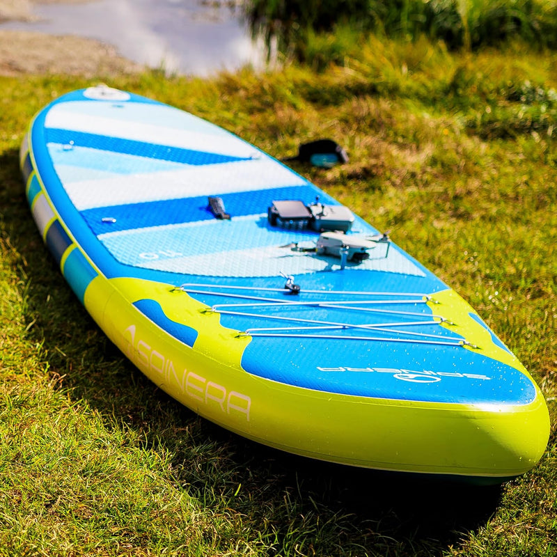 Close up of a blue paddleboard with yellow accents in some grass near a lake. 