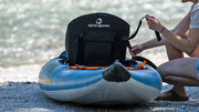 Woman tightening the straps of a seat in a blue kayak with orange and white accents by a river. 