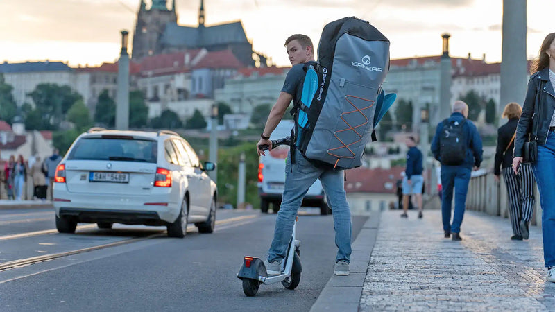 Man on a scooter carrying a large inflatable kayak on his back in a grey backpack.