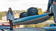 A woman and a man carrying an inflatable blue, orange, and white inflatable tandem kayak on a dock from each end. 