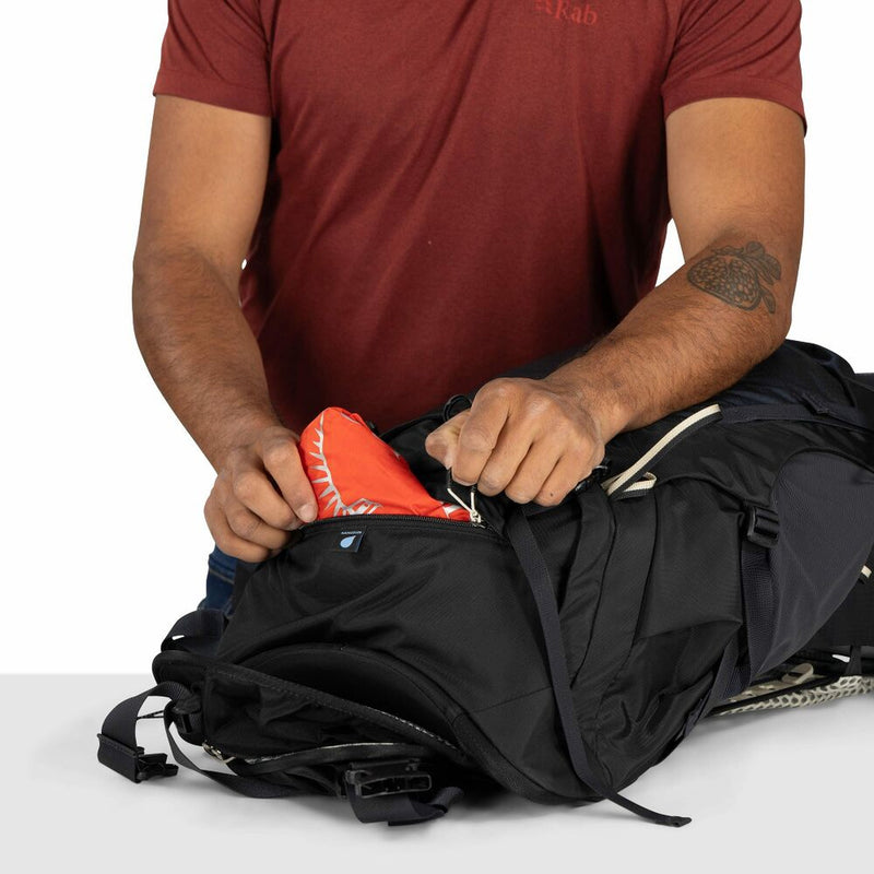 Person packing items into a black backpack on a white background