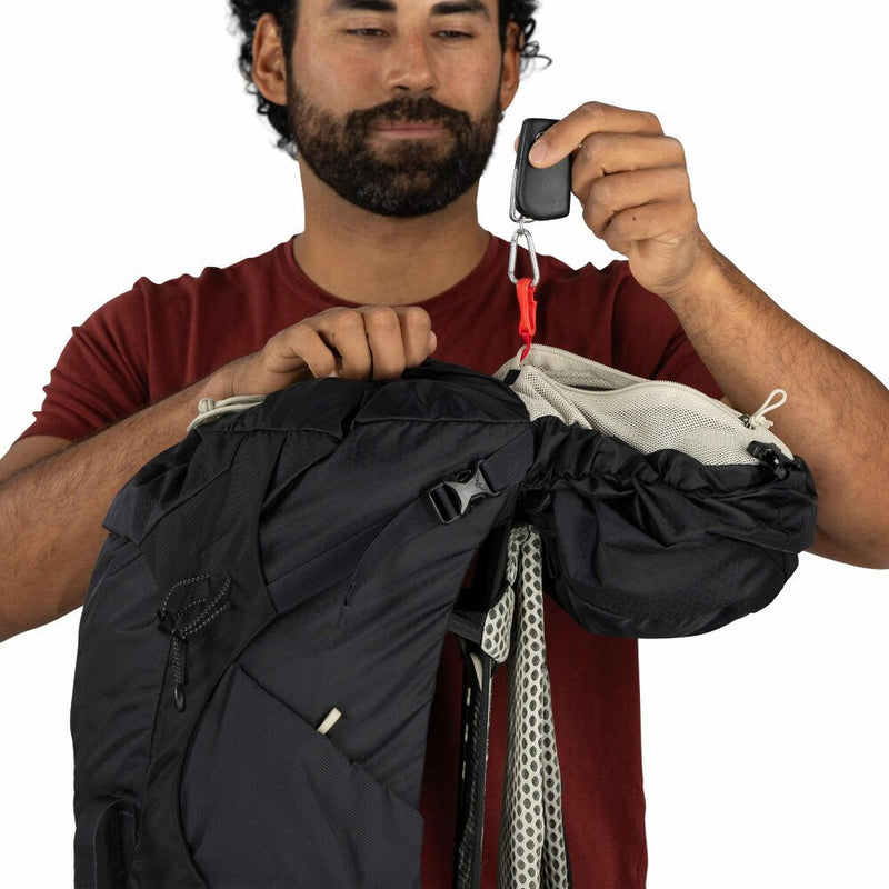 Man clipping his keys to a loop in a black backpack against a white background 