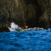 Person in a red coat paddling a yellow kayak in turbulent waters.