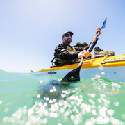 Man kayaking in clear water with a blue sky background