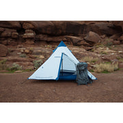 White and blue tent with hiking pack next to it in a canyon. 