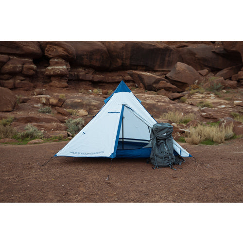 White and blue tent with hiking pack next to it in a canyon. 
