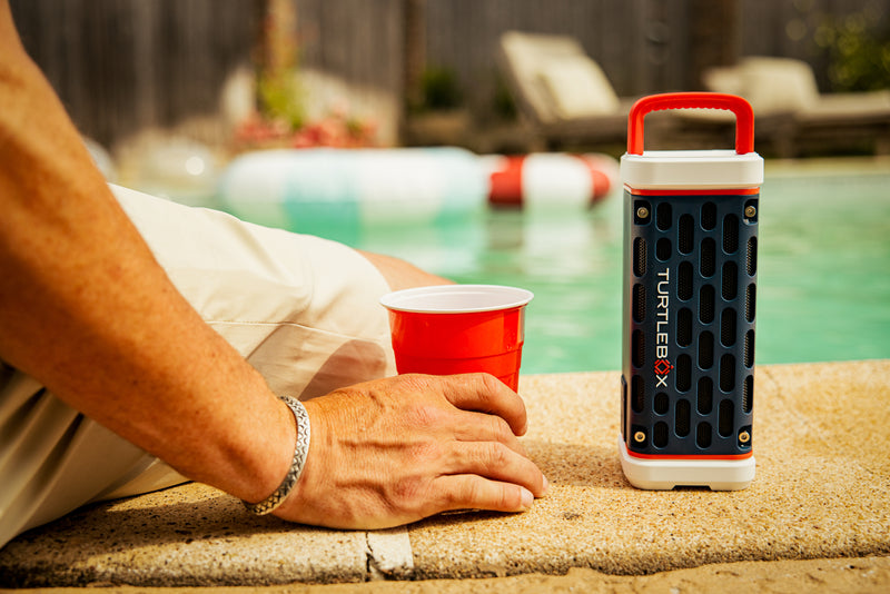 Person holding a red cup next to a portable speaker by a pool