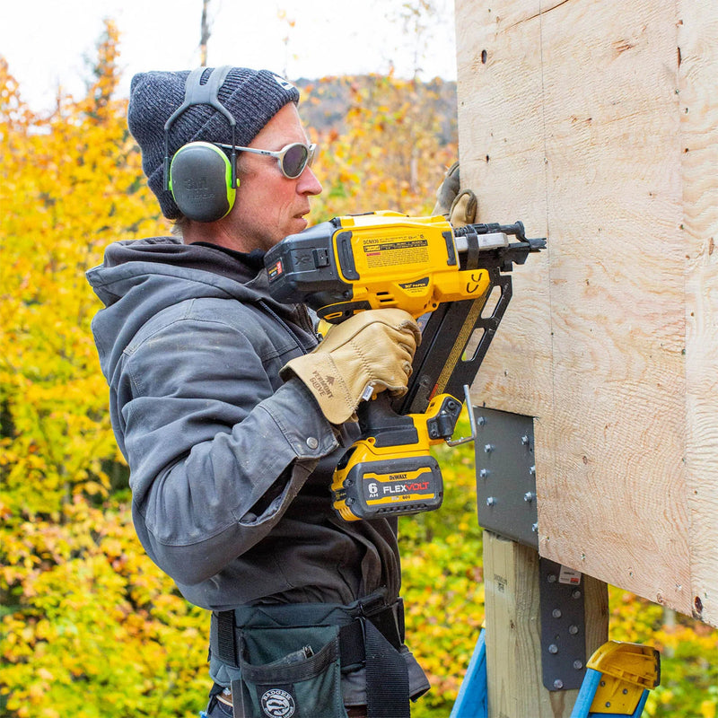 Person using a nail gun on a wooden structure with a blurred natural background