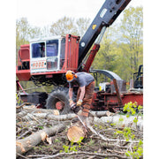 A worker wearing safety gear uses a chainsaw to cut logs in a logging operation, with a large red and black logging machine and trees in the background.