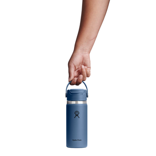 A hand holding the handle of a blue Hydro Flask insulated water bottle against a solid white background.